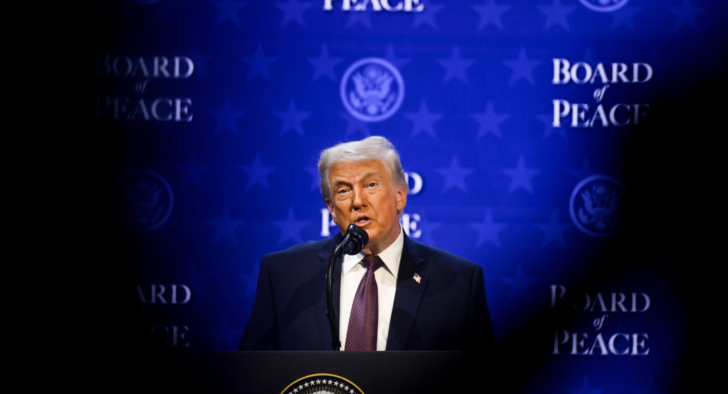 Trump stands in front of a blue screen reading "Board of Peace" 