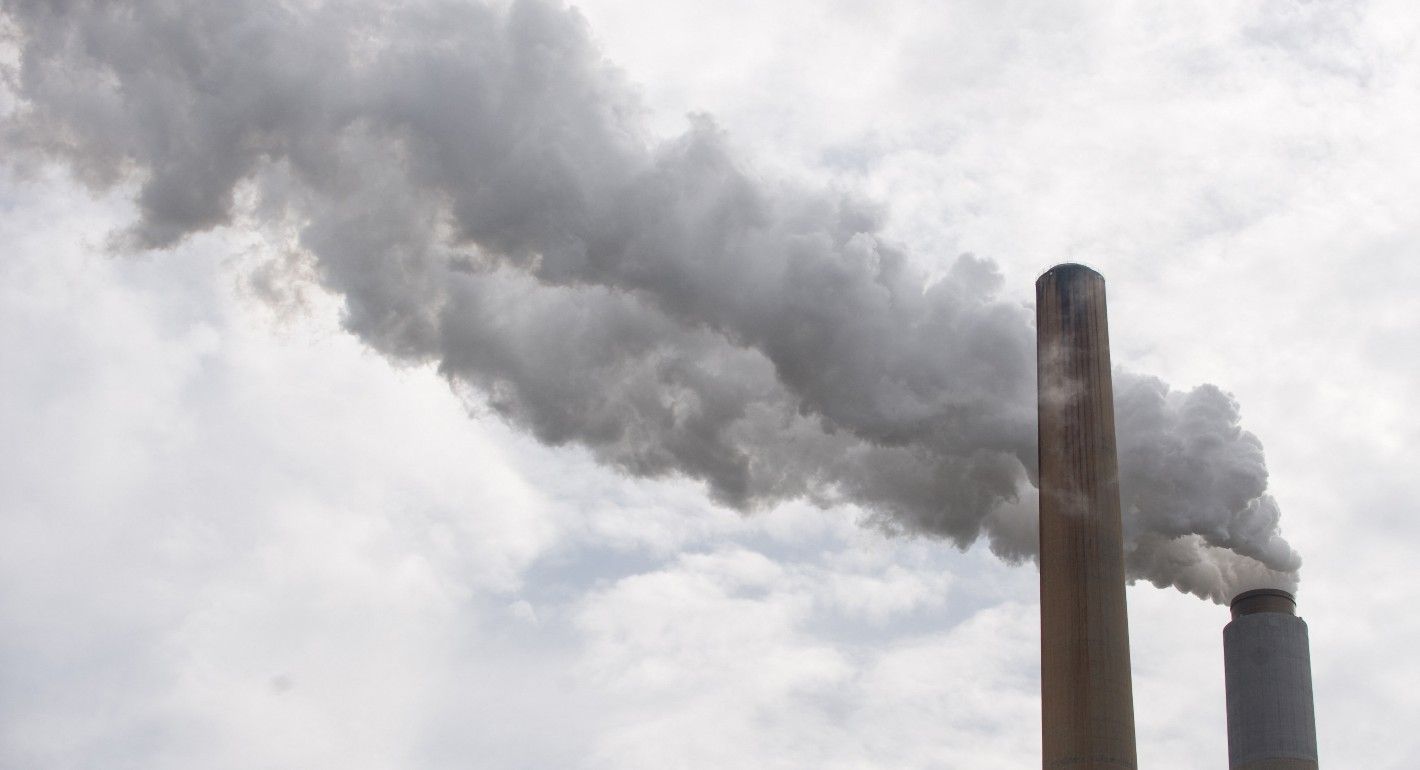 Two billowing clouds of carbon dioxide release from smoke stacks. The sky is light blue and cloudy.