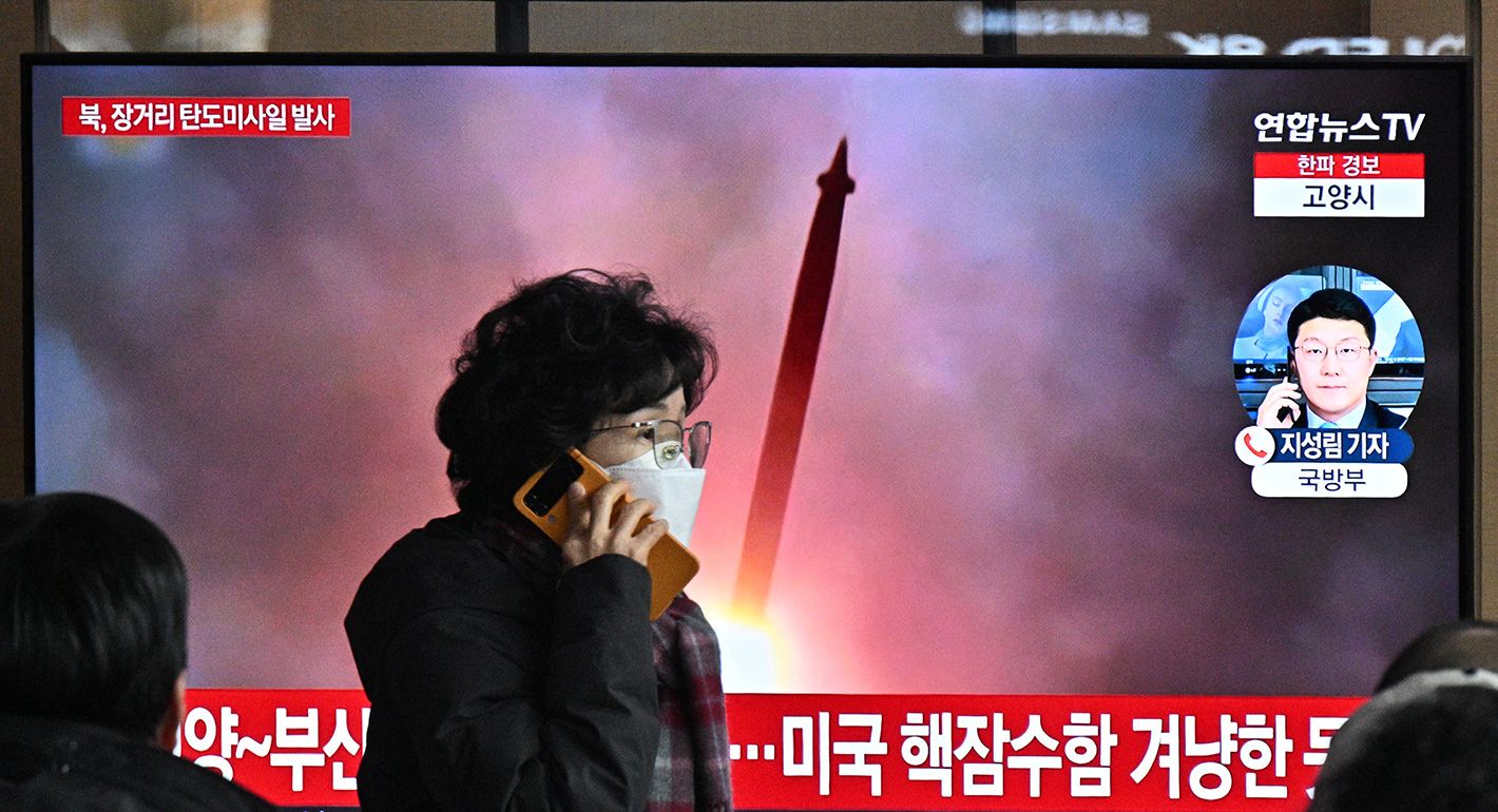 A woman walks past a television screen showing a news broadcast with file footage of a North Korean missile test, at a railway station in Seoul on December 18, 2023