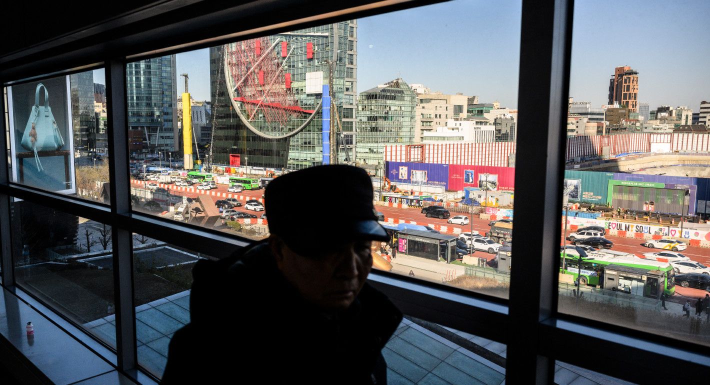A man walks by a window, his face shadowed, with the bustling city outside