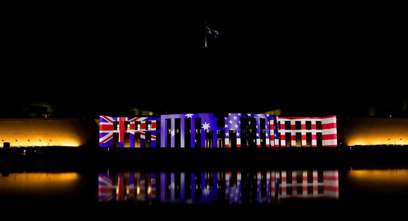 Australian Parliament House at night lit up with US, Australia, and NZ flags
