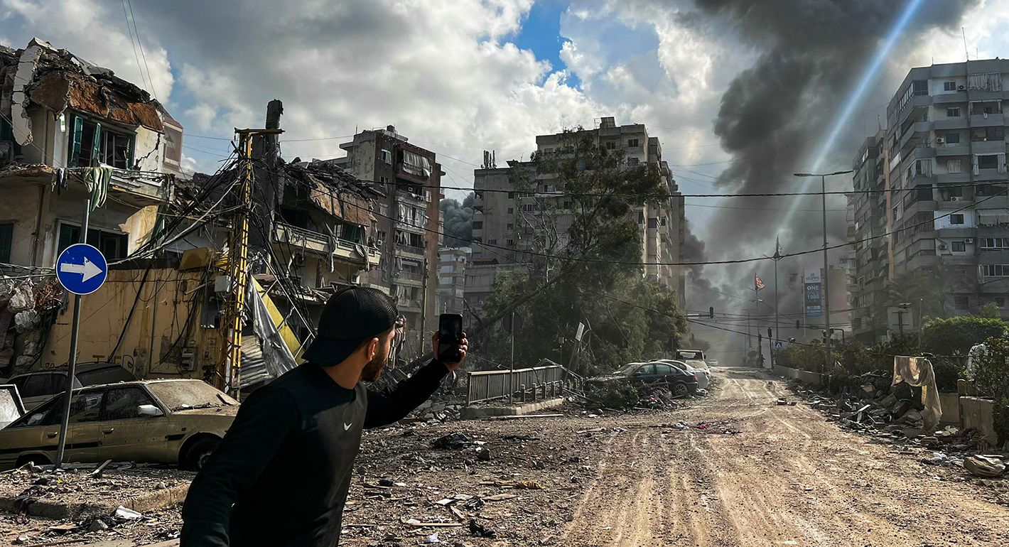 A man uses his mobile phone to take photos as smoke rises from the site of an Israeli airstrike targeting a neighborhood in southern Beirut on November 13, 2024, amid the ongoing war between Israel and Hezbollah. 