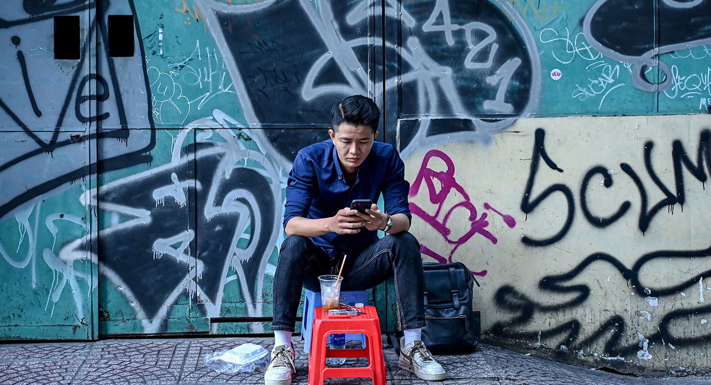 A man uses his smartphone as he sits on a sidewalk in Ho Chi Minh City on December 23, 2024. S