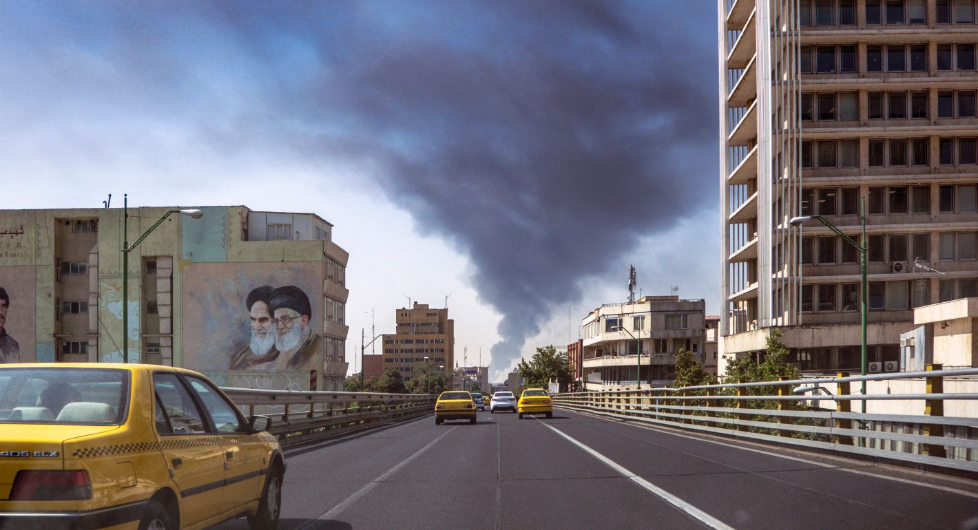 Cars driving along a road, with smoke rising in the distance