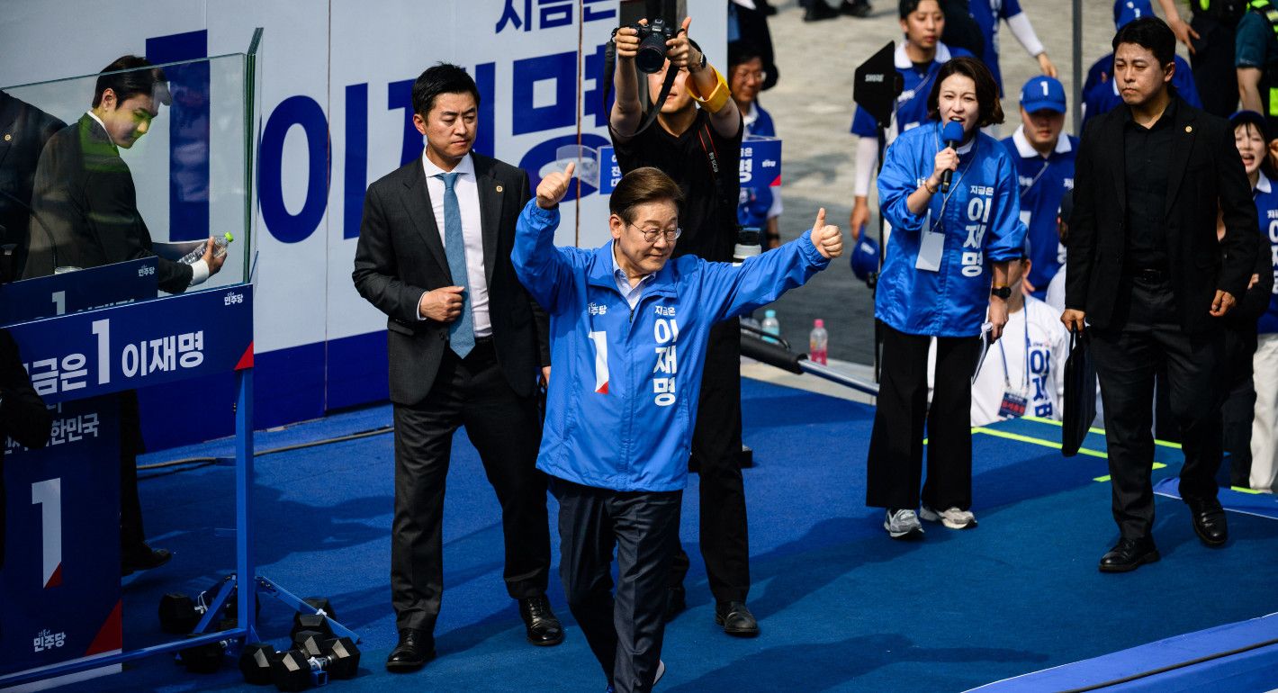 Man in a blue jacket on a stage waving