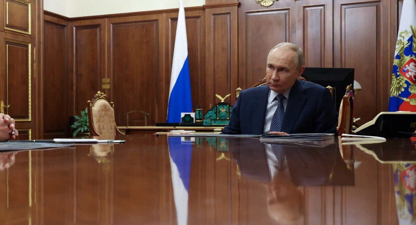 Putin sitting at a table talking with another man