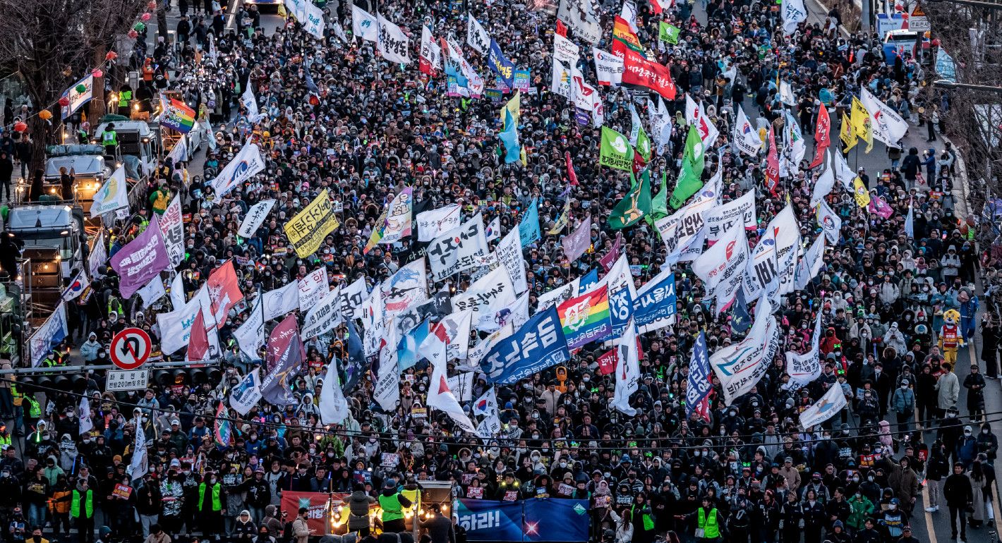 Photo of a crowd marching with flags against Yoon after his impeachment.